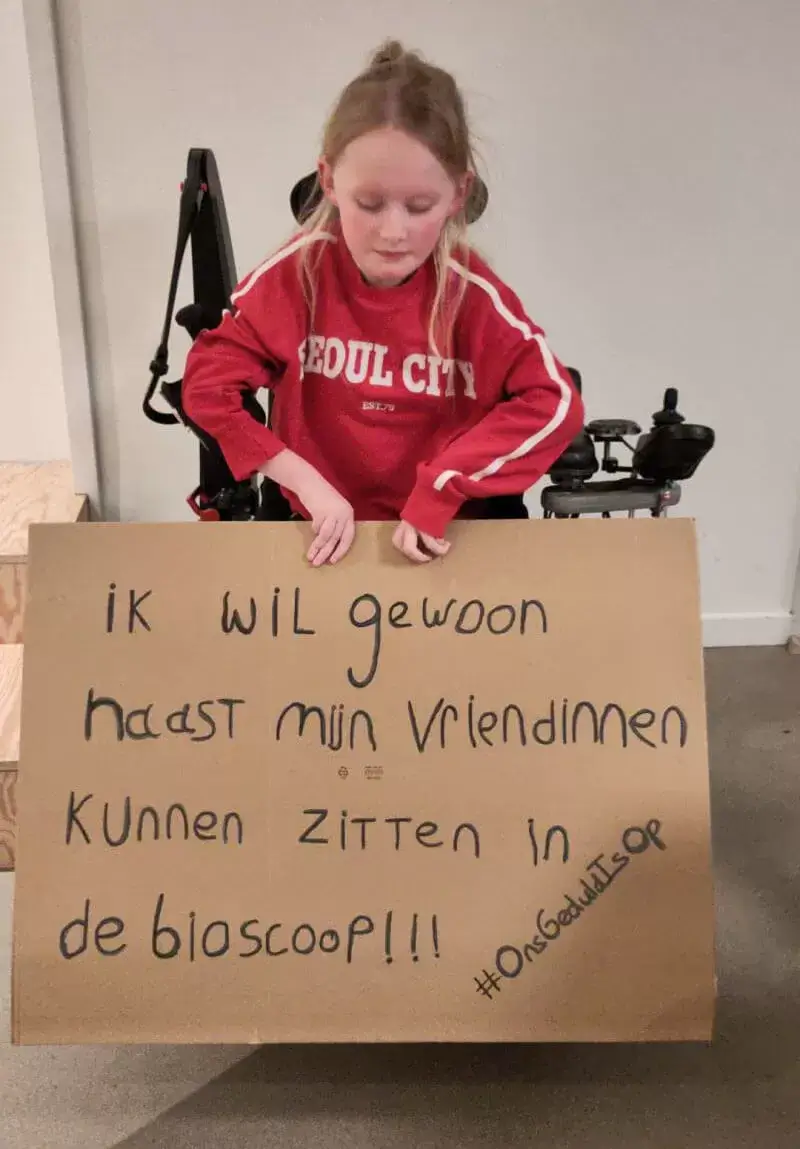 Signe zit in een rolstoel en houdt een bord vast met de tekst: Ik wil gewoon naast mijn vriendinnen kunnen zitten in de bioscoop! Ons geduld is op.