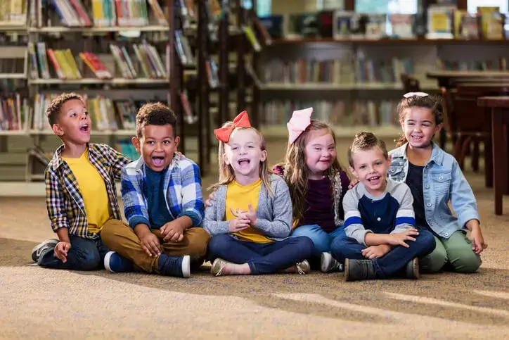 Zes kinderen met en zonder zichtbare beperking zitten naast elkaar op de grond.