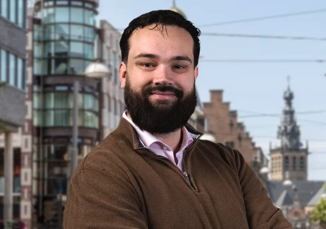Portret van Zino, een man met kort haar en een baard in een licht overhemd en bruin vest.
