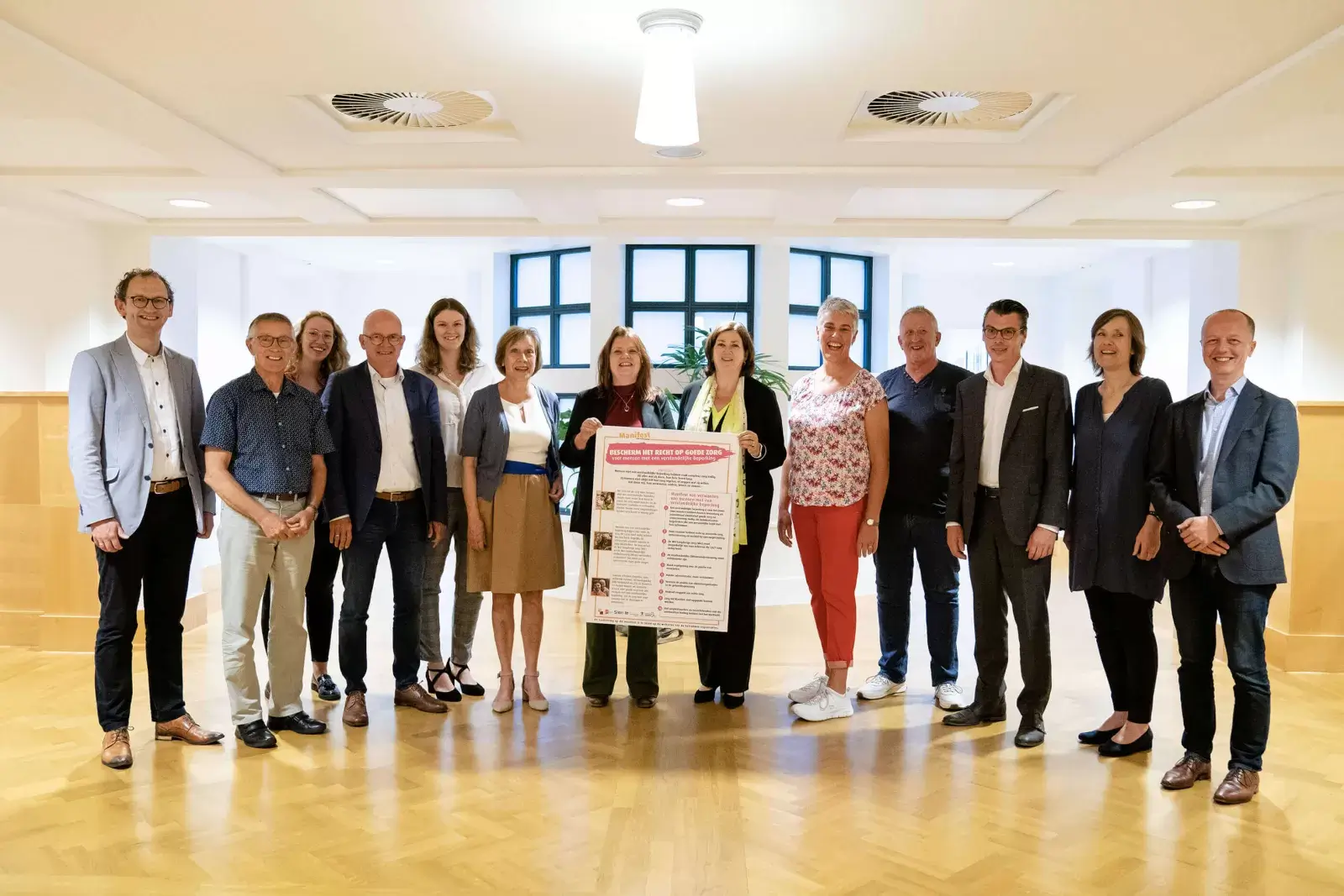 Dertien mensen staan rondom een groot plakkaat met daarop de tekst van het manifest. Twee van hen houden het plakkaat vast.