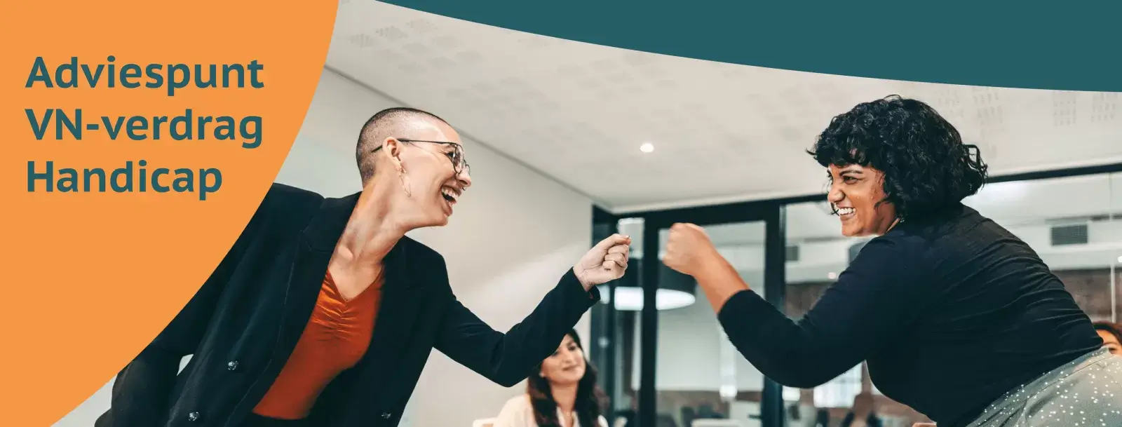 Een witter vrouw met kort haar en een licht getinte vrouw met zwart krullend haar leunen over een bureau om elkaar een boks te geven. Beide kijken vrolijk. Op de achtergrond zijn een glaswand en systeemplafond te zien.