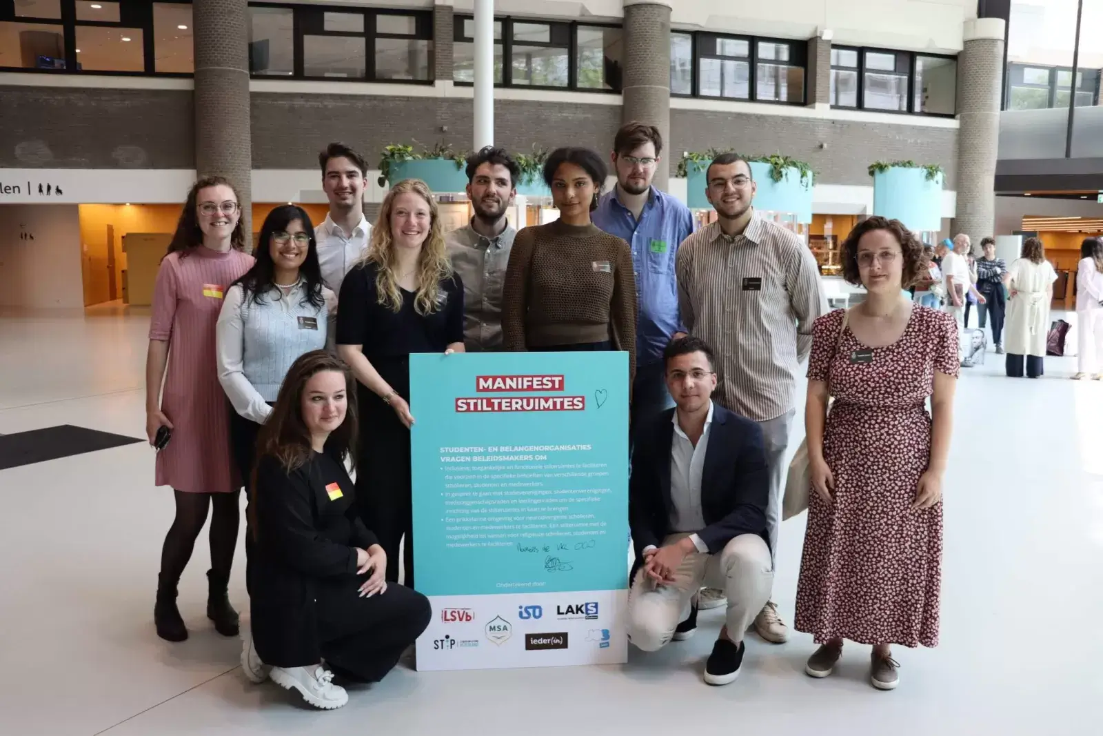Groep jonge mensen in de lobby van de tweede kamer staan rondom de aangeboden poster van het manifest.